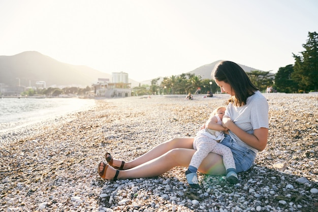 Maman est assise sur une plage de galets et allaite une petite fille