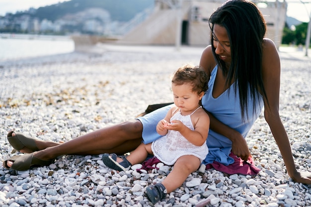 Maman est assise sur la plage avec une petite fille et la regarde