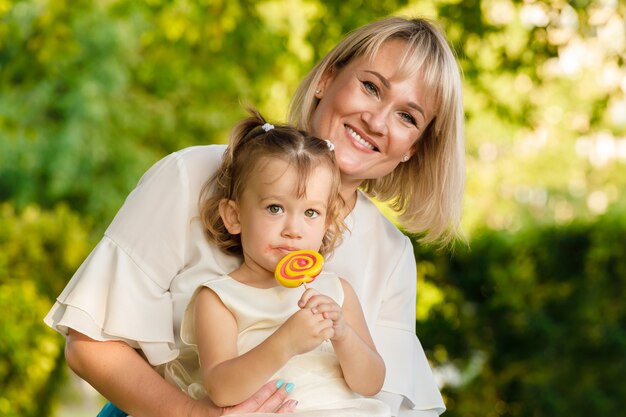 Maman est une blonde avec une fille dans ses bras qui a une douce sucette. dans le parc en été