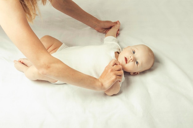 Maman fait de la gymnastique quotidienne à un petit bébé sur le lit avec un drap blanc. Mise à plat, vue de dessus.