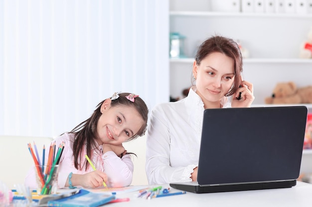 Maman femme d'affaires parlant sur mobile assise à la table de la pépinière