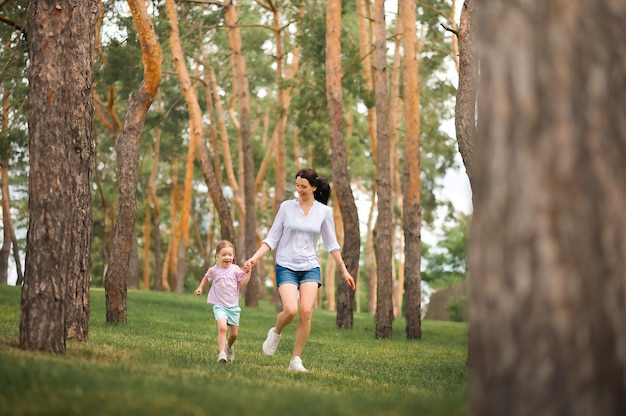 Maman et fille courent dans le gros plan de la forêt