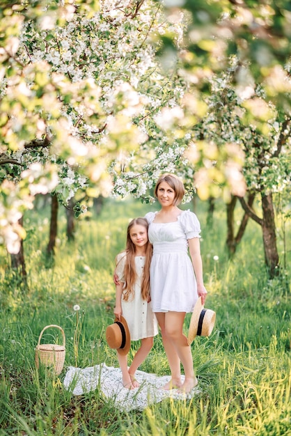 Photo maman et fille dans un jardin en fleurs de printemps ils se tiennent sur l'herbe verte et s'embrassent