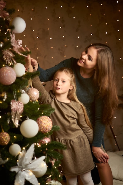 La maman et la fille heureuses décorent l'arbre de Noël sur le fond des guirlandes