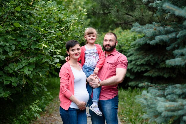 Une maman, une fille et un papa enceintes se promènent dans le parc.