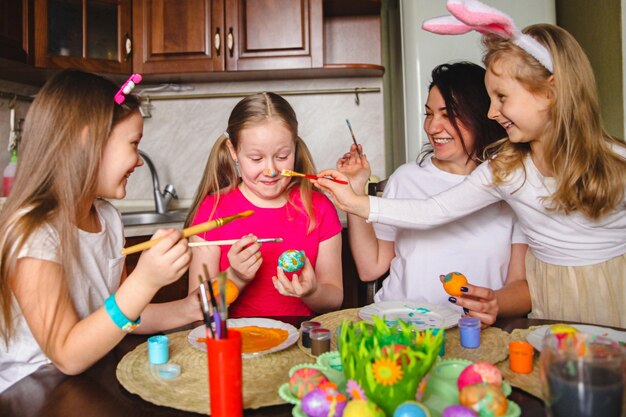 Maman et filles en train de colorier les œufs de Pâques se moquent de salir le nez de la fille.