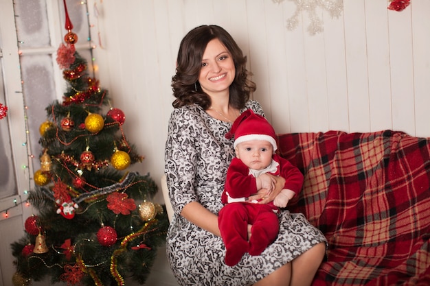 Maman et fils en costume de père Noël dans un cadre familial près d'un arbre de Noël contre un mur en bois blanc