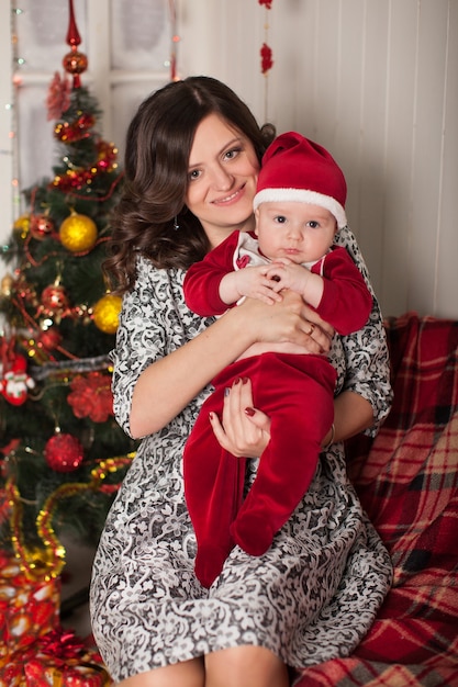 Maman et fils en costume de père Noël dans un cadre familial près d'un arbre de Noël contre un mur en bois blanc