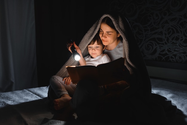 Maman et fils lisant un livre avec une lampe de poche sous la couverture