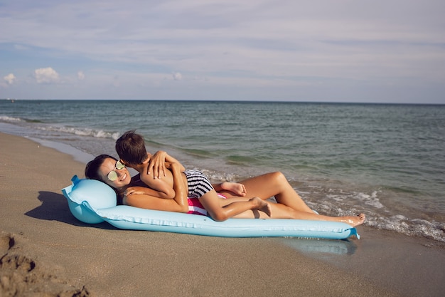 Maman et fils sont allongés sur la plage sur un matelas bleu gonflable pendant les vacances d'été
