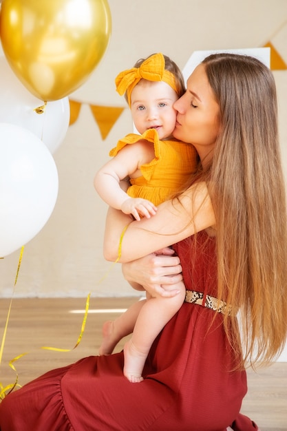 Une maman heureuse embrasse sa fille d'un an vêtue de vêtements jaunes, photo de studio pendant un an de l'enfant