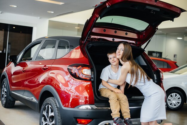 Une maman heureuse embrasse son fils après avoir acheté une nouvelle voiture chez un concessionnaire automobile