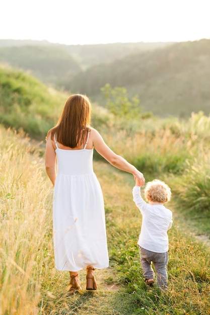 Maman heureuse avec petit fils marche par la main dans la nature