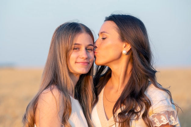 Une maman heureuse et sa fille adulte se tiennent ensemble près d'un champ de blé à la lumière du soleil du soir