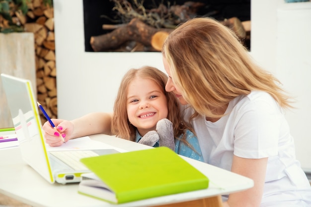 Maman heureuse avec sa fille assise dans le salon et dessinant ensemble