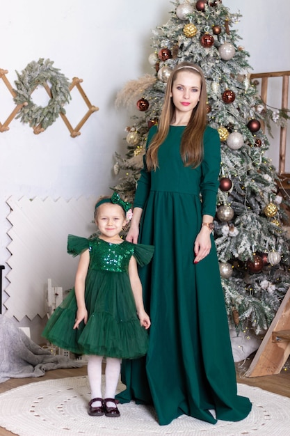 Une maman heureuse avec sa fille vêtue de belles robes vertes se tient près de l'arbre du nouvel an