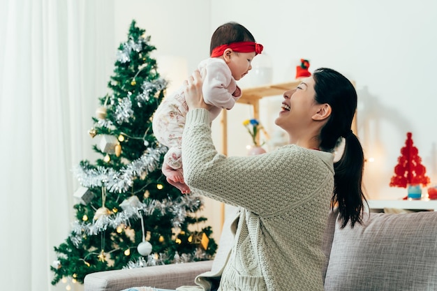 maman japonaise soulevant sa jolie petite fille et lui souriant. merveilleuse dame asiatique de vacances d'hiver remplie de bonheur avec son premier enfant. de vrais instants