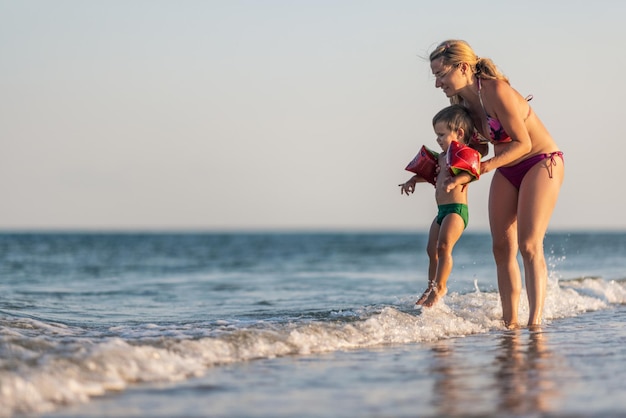 Maman jette son fils au-dessus de la mer pendant les vacances d'été sous le chaud soleil