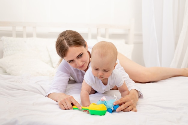 Maman jouant avec bébé 6 mois allongé sur un lit blanc, maman de loisirs avec bébé, place pour le texte