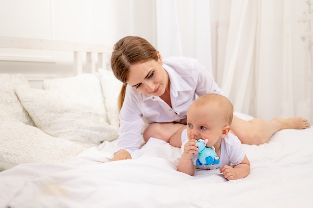 Maman jouant avec bébé sur un lit blanc