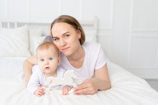 Maman joue avec bébé cheval jouet en bois sur le lit à la maison famille heureuse