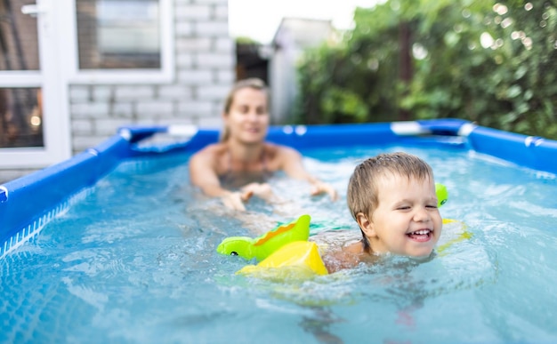 Maman joue avec un bébé nu en manches longues dans la piscine sur fond de coucher de soleil d'été