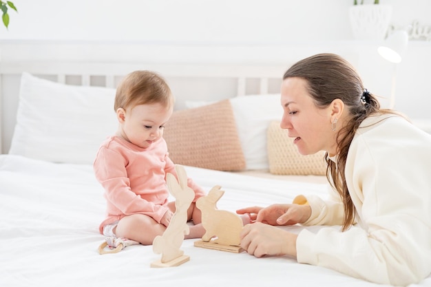 Maman joue avec sa petite fille avec des jouets en bois à la maison sur le lit et s'amuse avec la famille et la maternité