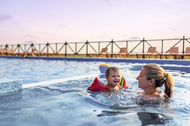 Maman joue avec son fils avec des manches dans la piscine en été