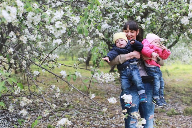 Maman avec des jumeaux sur un plaid en plein air dans un jardin de pommiers