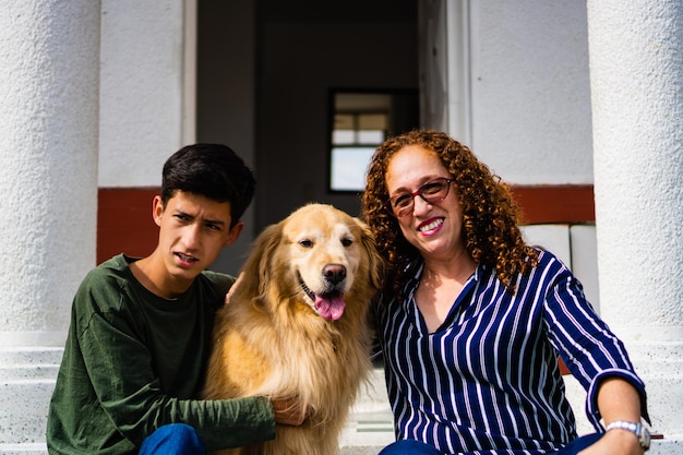 Maman latina avec son fils adolescent et son chien Golden retriever assis dans l'allée de leur maison