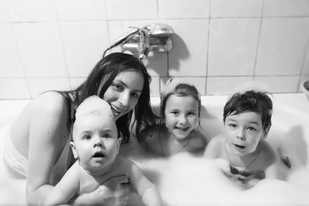 Maman lave les enfants. Maman et ses enfants suivent des procédures d'eau dans la salle de bain. Mousse, pulvérisation.