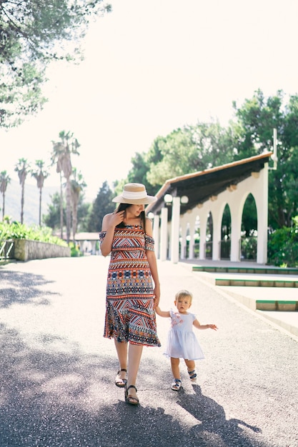 Maman marche en tenant la main d'une petite fille dans le parc verdoyant