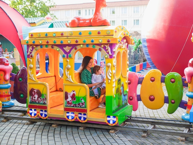 Maman monte dans un train pour enfants avec un enfant. Maman monte avec un enfant sur un carrousel. Portrait d'une heureuse mère et fils à cheval sur un carrousel