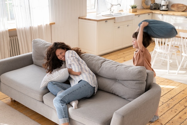 Maman ou nounou a une drôle de bataille d'oreillers avec un petit garçon en pause du travail à distance ou le week-end à la maison