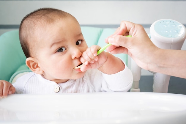 Maman nourrit le bébé avec une cuillère de purée de légumes à la table d'alimentation des enfants Appétit du bébé nutrition saine introduction d'aliments complémentaires Copyspace mock up