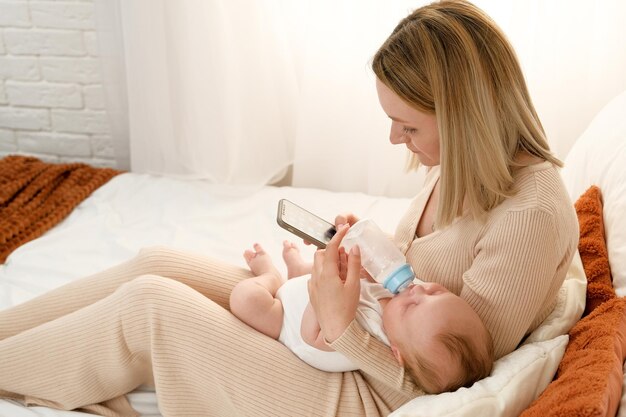 Maman nourrit un nouveau-né avec des biberons de lait maman tient le téléphone tout en nourrissant le bébé