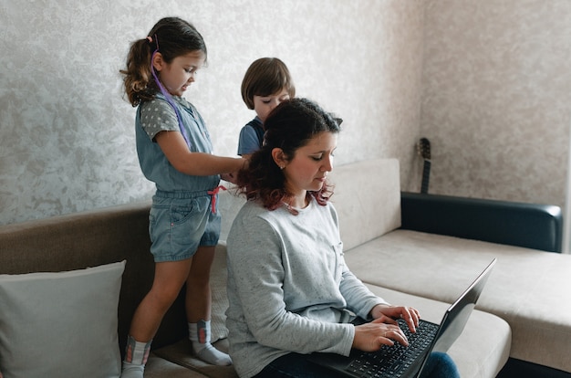 Une maman occupée essaie de travailler sur un ordinateur entourée de deux jeunes enfants. travail à distance