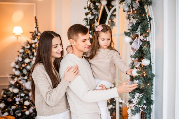 Maman, papa et fille décorent la maison pour Noël. Portrait d'une famille sur fond de nouvel an