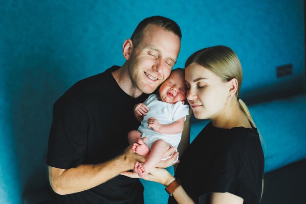 Maman et papa heureux tiennent leur nouveau-né dans leurs bras Jeune mère et père embrassent un nouveau-né Jeune famille et nouveau-né à la maison