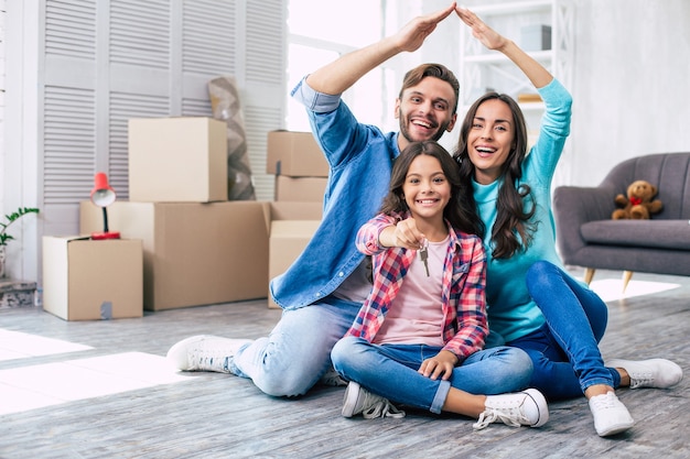 Maman et papa imitent un toit de la maison avec leurs mains tandis que leur fille tient les clés de leur nouvel appartement dans ses mains. Concept de déménagement de maison