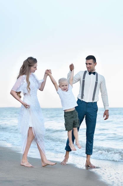 Maman et papa lèvent les mains de l'enfant Jeune famille se promène sur la plage Parentalité heureuse et enfance Cadre vertical