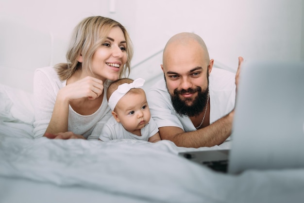 Maman papa et une petite fille caucasienne de 6 mois le soir s'allongent sur le lit dans la chambre et communiquent par appel vidéo