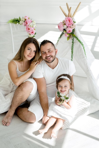 Maman et papa avec une petite fille sont assis à côté d'un wigwam avec des fleurs