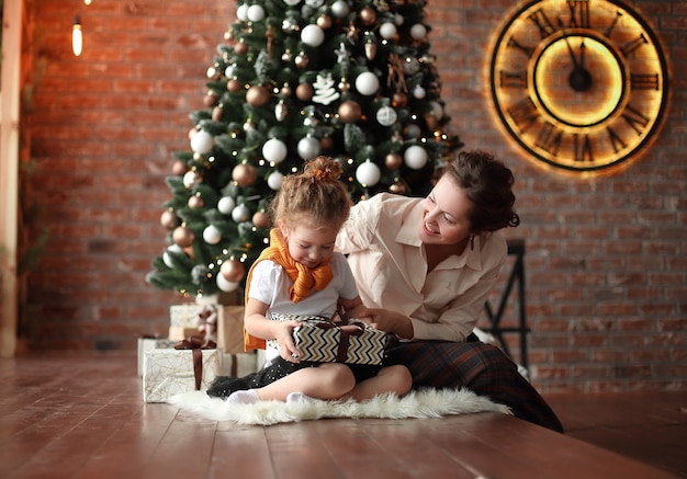 Maman parle à sa petite fille, assise près de l'arbre de Noël.