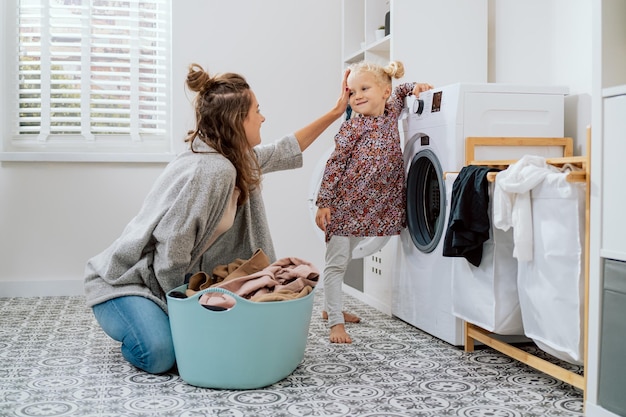 Maman passe du temps avec sa fille dans la buanderie tout en faisant les tâches quotidiennes