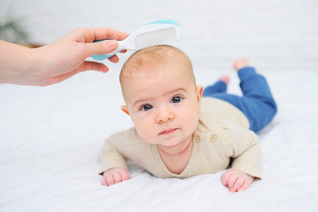 Maman peigne le bébé avec une brosse à cheveux spéciale sur blanc