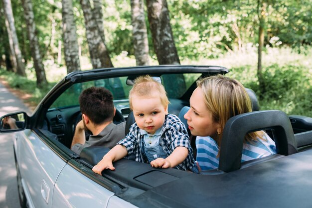 Maman, père et petit fils dans une voiture décapotable, voyage familial d'été dans la nature.