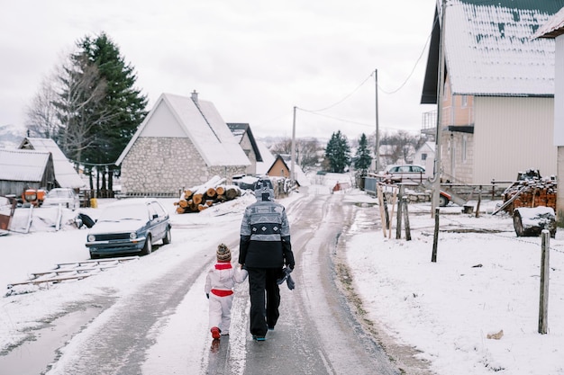 Maman et une petite fille se tiennent la main le long d'une route glacée dans une vue arrière du village