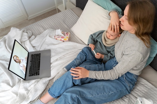 Photo maman prenant soin de son enfant et téléconsultation avec un médecin