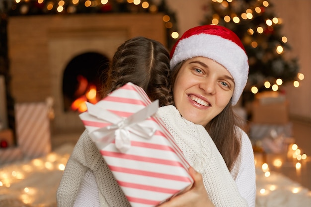 Maman de race blanche remercie son petit enfant pour la boîte-cadeau, étreignant sa fille, posant près de l'arbre de Noël à la maison